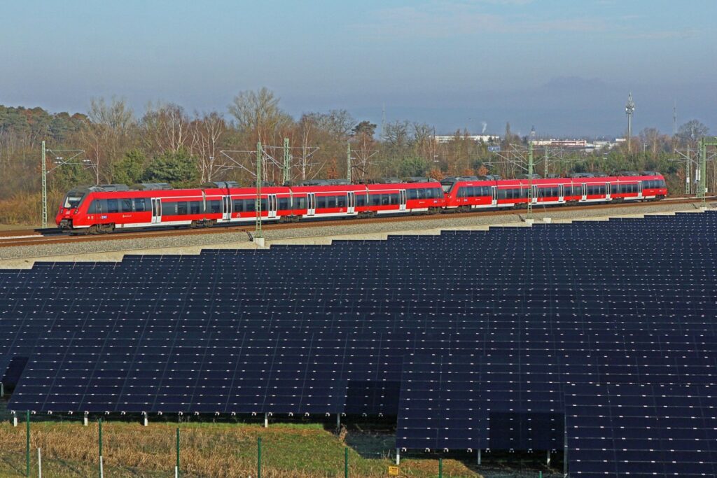 Photovoltaik-Anlage an einer Bahnstrecke mit dahinterfahrenden Regionalexpress