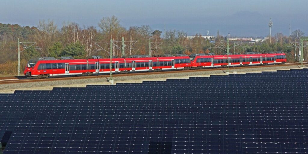 Photovoltaik-Anlage an einer Bahnstrecke mit dahinterfahrenden Regionalexpress