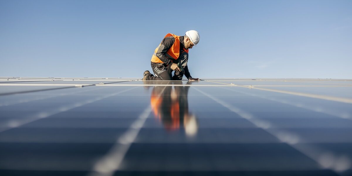 A handyman on the rooftop installing solar panels.